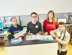 Eine youngCaritas-Mitarbeiterin im Büro einer Kommunikationsberatung und Mediengestaltung mit zwei Mitarbeitern der Firma und einem Teilnehmer des "youngHeroes Day"