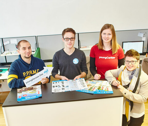 Eine youngCaritas-Mitarbeiterin im Büro einer Kommunikationsberatung und Mediengestaltung mit zwei Mitarbeitern der Firma und einem Teilnehmer des "youngHeroes Day"