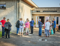 Menschen versammeln sich vor einem Gebäude in Böheimkirchen, um Hochwasser-Soforthilfe von Caritas zu erhalten. Ein Schild mit der Aufschrift "Caritas Wir helfen" ist sichtbar, während die Menschen in einer lockeren Gruppe stehen und miteinander sprechen.