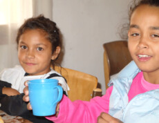 Zwei Mädchen im Kinderzentrum Eden, eines hält eine blaue Tasse, beide wirken entspannt und zufrieden.